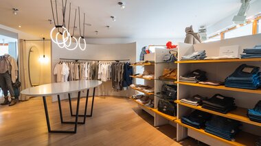 Interior of a clothing store with racks of clothes, shelves with folded apparel, and modern lighting. | © Johannes Radlwimmer