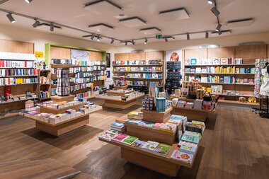 Inside view of a well-stocked bookstore with wooden tables and shelves filled with books. | © Johannes Radlwimmer