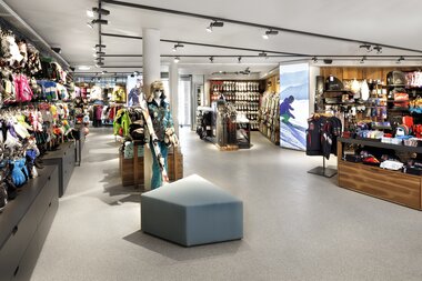Interior of a sports store with sports gear, clothing, and accessories on shelves and tables. | © Christian Wöckinger