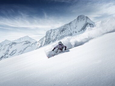 Skier carving through deep snow in mountain terrain with cloudy sky. | © Kitzsteinhorn