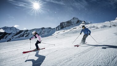 Skieriders on a glacier ski slope under a cloudy sky with the sun shining | © Kitzsteinhorn
