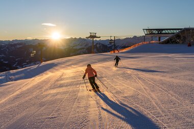 Skier person on a snowy slope at sunset with mountain view in the background. | © Schmittenhöhe