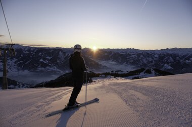 Skier on a snowy slope at sunset with mountain scenery in the background. | © Zell am See-Kaprun Tourismus