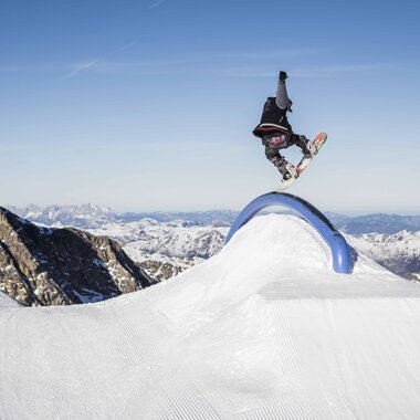 Person skateboarding in the snow park with mountain scenery in the background. | © Roland Haschka