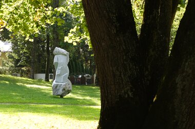 A sculpture is located in a park, surrounded by trees and green grass.