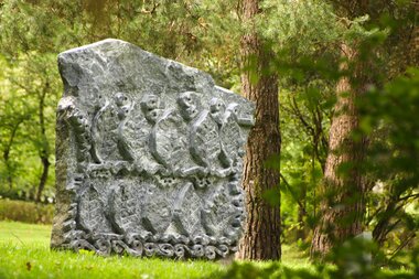 Stone sculpture in the sculpture park depicting relief-like figures, surrounded by trees and grass