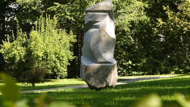 Large abstract stone sculpture in a green park with trees and grass.
