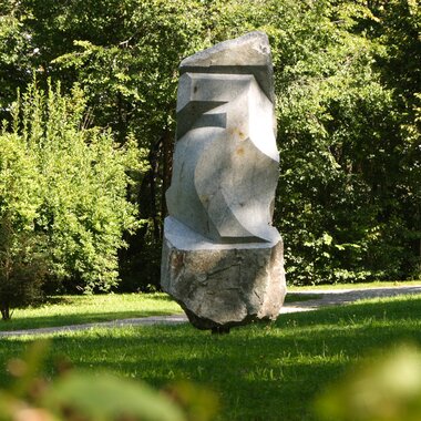 Large abstract stone sculpture in a green park with trees and grass.