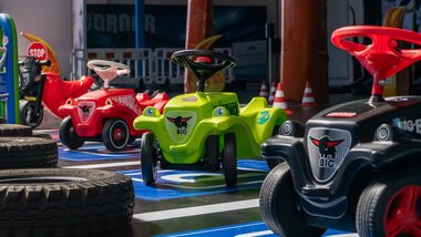 Various colorful children's ride-on cars in an indoor park, with tires in the foreground and a playful atmosphere. | © Schmittenhöhe
