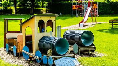 Playground with wooden train, tunnels, and slide in a park on a sunny day | © Zell am See-Kaprun Tourismus