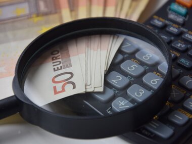 A 50 euro banknote is viewed with a magnifying glass on a calculator.