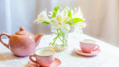 Ceremonial teapot and cups with flowers in a glass vase on a set table.