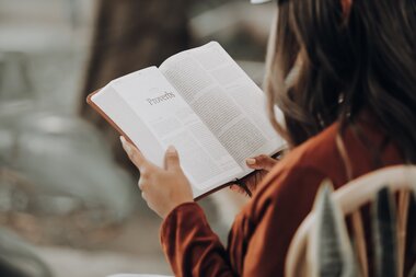 Person reading an open book outdoors, focusing on hands and the book.