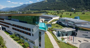 Modern spa and hotel complex amidst green landscape with mountains in the background under a bright blue sky. | © TAUERN SPA Zell am See-Kaprun