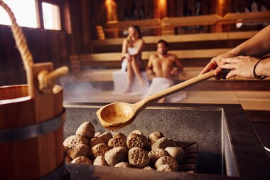 Relaxing spa sauna scene with hot stone bath and people sitting on benches in the background. | © TAUERN SPA Zell am See-Kaprun