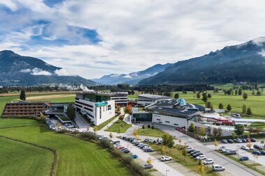 Exterior view of Tauern Spa in Kaprun with mountains in the background and parked cars in the foreground. | © TAUERN SPA Zell am See-Kaprun