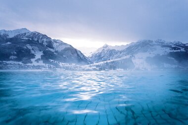 A winter mountain landscape with an icy lake and snow-covered mountains in the background. | © TAUERN SPA Zell am See-Kaprun