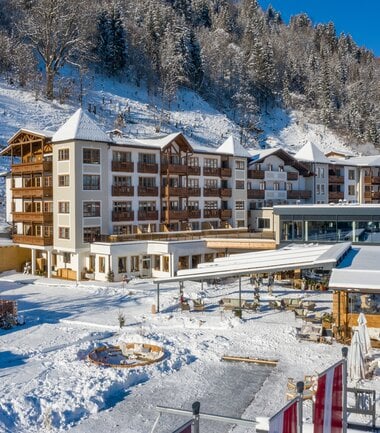 Multi-story hotel in a winter mountain landscape with snow-covered ground and forest in the background. | © Hotel Alpenblick