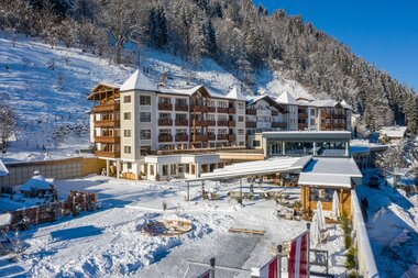 Multi-story hotel in a winter mountain landscape with snow-covered ground and forest in the background. | © Hotel Alpenblick