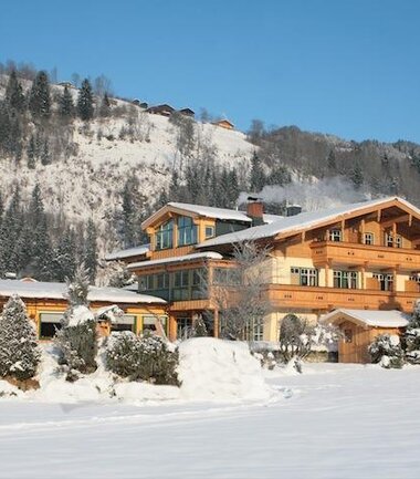 A large guesthouse in a snowy landscape, surrounded by snow-covered trees and mountains. | © Gästehaus Trixl