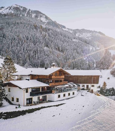 Cozy accommodation set against a snowy winter landscape in the mountains, sunlight breaking through clouds. | © Panorama Ferienhaus Guggenbichl