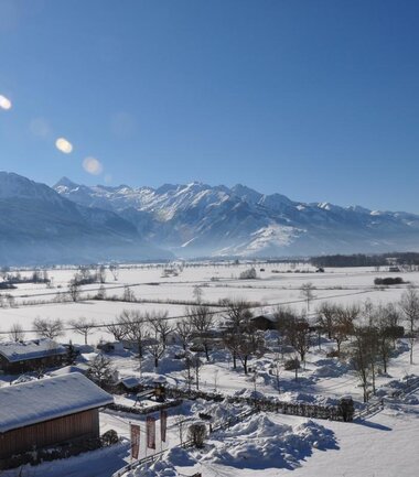 Panoramic view of a snowy valley with mountains in the background, with buildings and trees in the foreground. | © Panorama Camp Zell am See