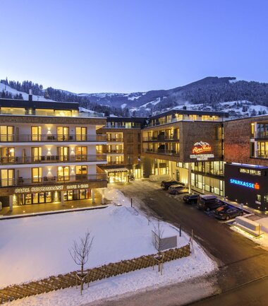 Alpenparks Hotel Central during winter evening, illuminated buildings against a snowy backdrop, surrounding mountains, peaceful scene. | © Alpenparks Hotel Central