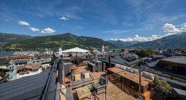 Rooftop terrace with seating, overlooking the city and mountains on a sunny day. | © Hotel Heitzmann Zell am See