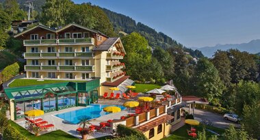 Multi-story hotel surrounded by lush nature with a pool and lounge chairs in the foreground. | © Hotel Berner Zell am See