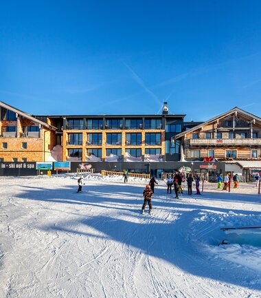 The Berghotel Schmittenhöhe in winter with snowy surroundings and several guests outside, engaging in skiing or walking. | © Berghotel Schmittenhöhe