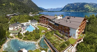View of a hotel with two pools in a mountainous landscape with a lake in the background. | © Hotel Salzburgerhof