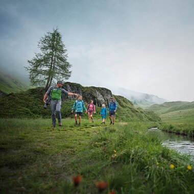 Group hiking on a green hillside with a stream and forests in the background. | © Kitzsteinhorn